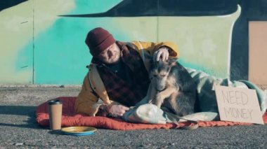A beggar and his dog are lying on the ground near a graffiti wall