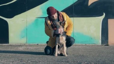 A beggar is petting his dog next to the graffiti wall