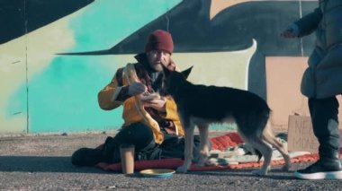 Stranger gives money to a beggar and a dog eating in the street
