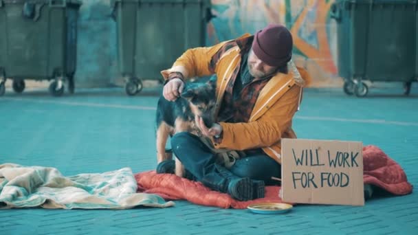A beggar is feeding his dog while sitting on the ground — Vídeo de Stock
