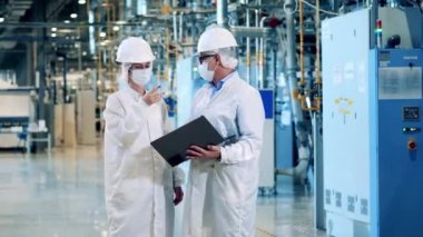 Two plant engineers are talking about plans in face masks