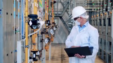 Male inspector with a laptop is observing plant pipes