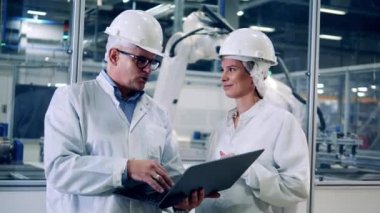 Two plant engineers are talking near robotic machines at work