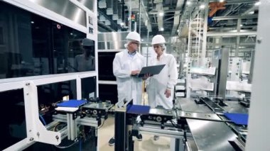 Two engineering experts are observing conveyor with solar cells