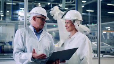 Two plant inspectors are talking near moving robotic machines