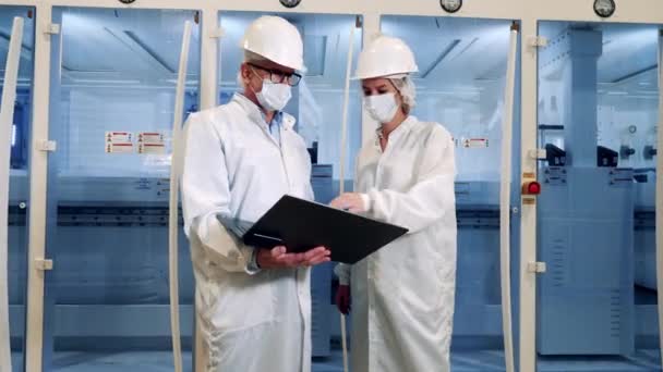 Dos inspectores en máscaras faciales están hablando cerca de modernas máquinas de planta — Vídeo de stock