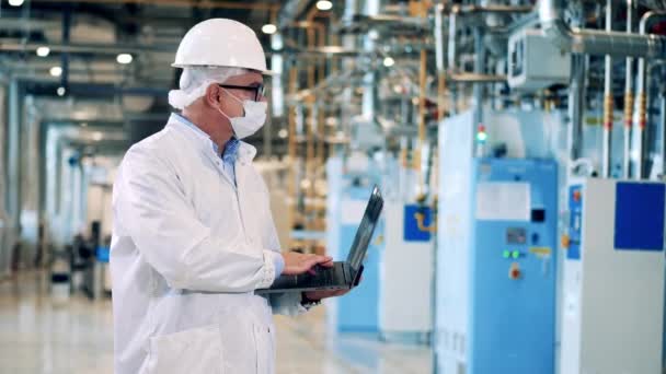 Male engineer in a hardhat is using his laptop in the factory — Stockvideo