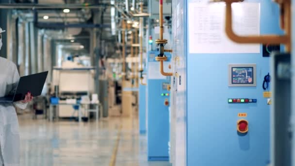 Female engineer with a laptop comes closer to the factory machines — Video