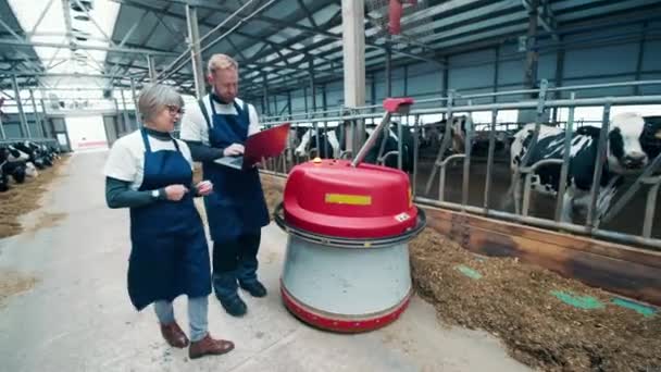 Two experts are following a feed pusher through the farm — Vídeo de stock