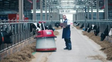 Çiftlik hayvanları çiftçisi çiftlikte çalışan bir robotu gözlemliyor.