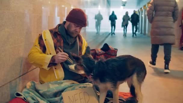 Um mendigo está tratando seu cão enquanto come macarrão — Vídeo de Stock