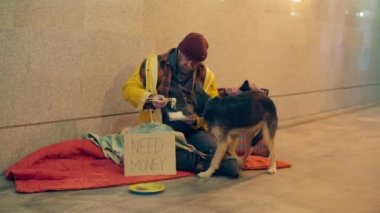 Evsiz biri yerde otururken köpeğini tedavi ediyor.