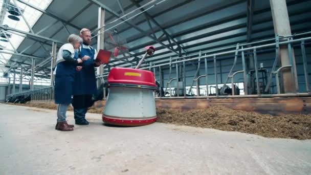 두 명의 가축 농부가 일하는 농업용 로봇을 관찰하고 있다 — 비디오
