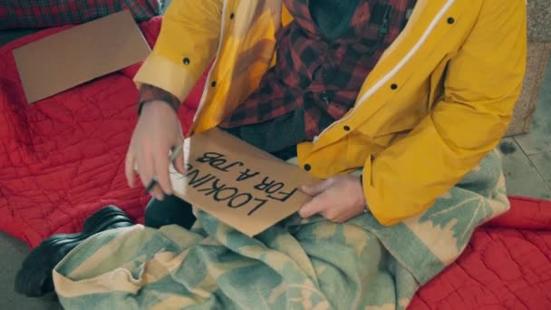 Ein Obdachloser schreibt auf einen Teller, dass er einen Job sucht — Stockvideo