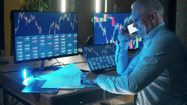 En börsmäklare pratar i telefon bredvid datorer. — Stockvideo