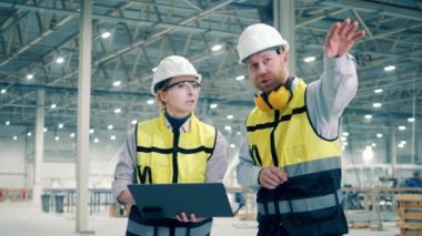 Güvenlik giysisi giymiş iki fabrika işçisi birbiriyle konuşuyor. Fabrika işçileri, endüstriyel, teknoloji, üretim kavramı.