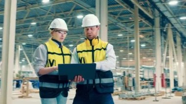 Fiberglas fabrikasında iki işçi etrafa bakıyor ve konuşuyor.