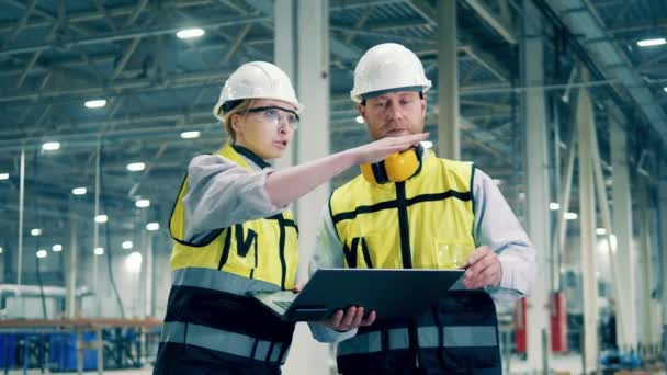 En man och en kvinna i skyddskläder diskuterar fabriken. Modern fabrik, ingenjörer som arbetar på industrianläggning. — Stockvideo