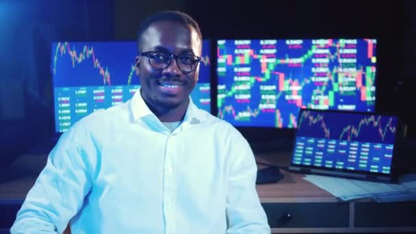 Courtier africain est assis à côté des moniteurs avec des diagrammes de stock — Video