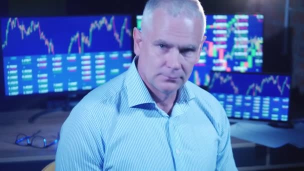 Мужской брокер рядом с мониторами, показывающими данные фондового рынка — стоковое видео