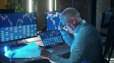 Erkek tüccar, borsa raporlarını incelerken telefonda konuşuyor.