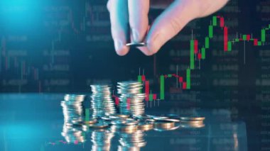 A hand adds coins to a pile with currency rates in the background