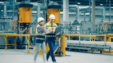 İki işçi fiberglas fabrikasında yürüyorlar ve konuşuyorlar.