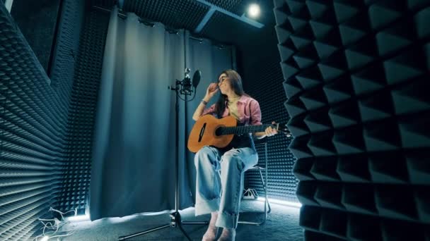 Женщина играет на гитаре и поет в студии звукозаписи — стоковое видео