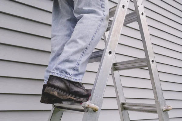 Male worker standing on stepladder in front of house siding