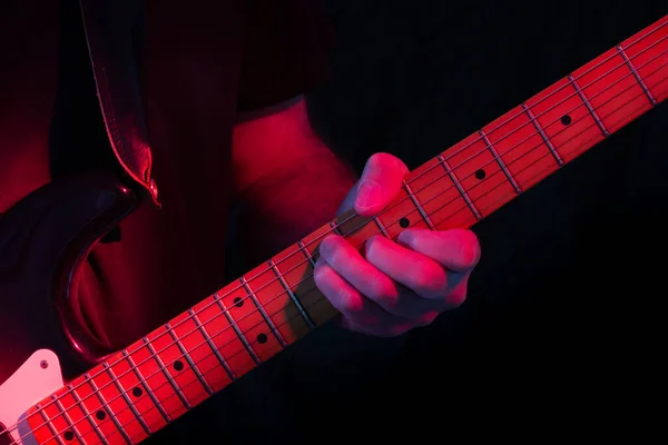 Electric guitar player in red stage lighting with dark to black background. Low key shot.