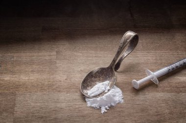 Drug addiction concept with spoon, syringe and white powder on wood