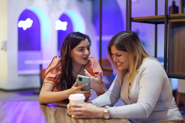 Arkadaşları cep telefonuna bakıyor ve mor arka planlı bir kafede gülümsüyor. Yüksek kalite fotoğraf