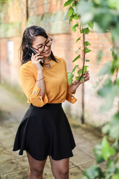 Young brunette Latin American woman talking on the phone touching plant . High quality photo
