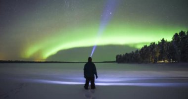 Timelapse of person watching aurora borealis during strong bright green northern lights display in unique amazing travel experience. Time lapse in Lapland, Finland