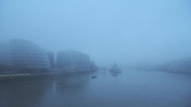 Foggy and misty River Thames in London on Coronavirus Covid-19 lockdown day one, in atmospheric weather with moody blue mist and fog around HMS Belfast and City Hall by Tower Bridge, England, UK