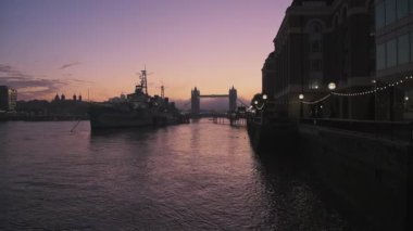 Tower Bridge in London with beautiful colourful sunrise, dramatic clouds and purple sky, showing iconic famous skyline and HMS Belfast on day one of Coronavirus Covid-19 lockdown in England, UK
