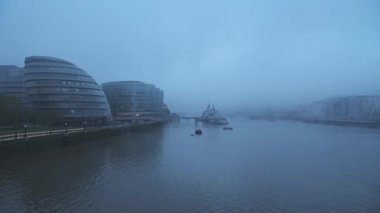 Foggy and misty River Thames in London on Coronavirus Covid-19 lockdown day one, in atmospheric weather with moody blue mist and fog around HMS Belfast and City Hall by Tower Bridge, England, UK