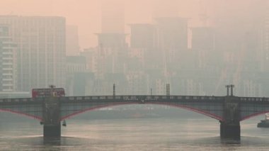 Central London City Skyline with iconic red London bus driving over Lambeth Bridge in atmospheric orange sunset with mist and fog, shot in Coronavirus Covid-19 lockdown in England, UK