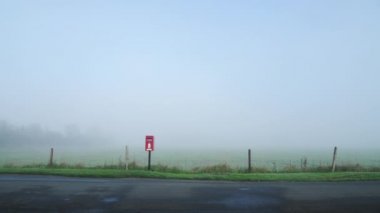 Iconic red English post box, postbox in a village in the countryside by the road in England with thick fog and mist with misty foggy weather conditions, traditional rural scene in England, UK