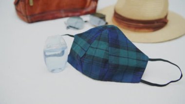 Home made coronavirus face mask with plaid pattern, small bottle of hand sanitizer and travel items in background, flat lay, concept