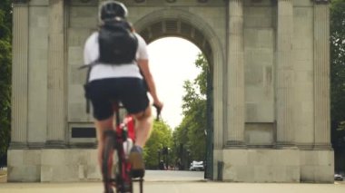Cyclist with helmet and backpack rides bicycle through stone arch in park