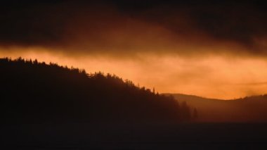 Panoramic landscape view of a bright orange sunrise over a frozen lake, on a misty morning, in Lapland, Finland