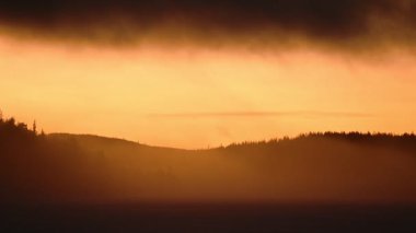 Landscape view of a bright orange sunrise over a frozen lake, on a misty morning, in Lapland, Finland