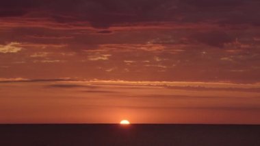 Sun going behind the ocean on a bright red and orange sunset, with few clouds
