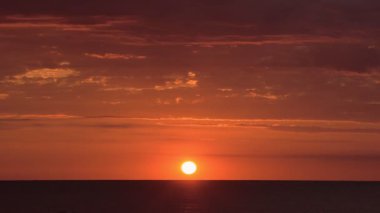 Bright red and orange sunset landscape view over the ocean, with few clouds