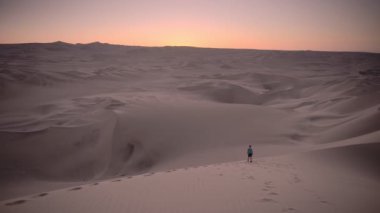Landscape view of a man looking at the sunset from a desert dune, Peru