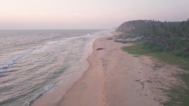 Aerial view of Varkala coastline with waves crashing on the sandy beach, in Kerala, India, at dusk