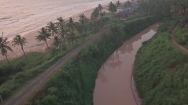 Aerial view of a river flowing near palm trees and Varkala coastline, in Kerala, India, at dusk
