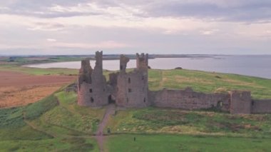 Dunstanburgh Castle at sunset in Northumberland, England, UK. Aerial drone reveal