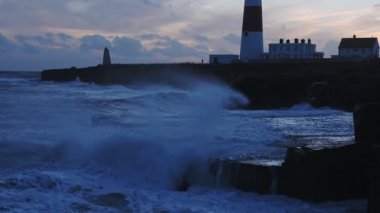 Stormy waves crashing on the coastline near Portland Bill lighthouse, at sunset